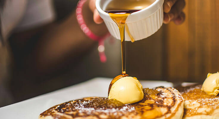 Pouring syrup on buttered pancakes.