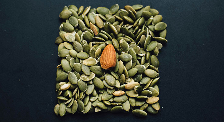 Almond surrounded by pumpkin seeds on dark background.