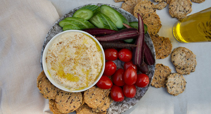 Hummus, vegetables, crackers on plate with olive oil.