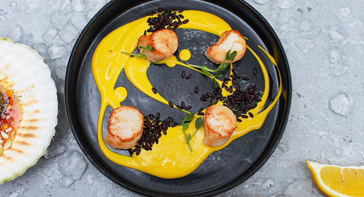 Gourmet scallops on black plate with sauce.