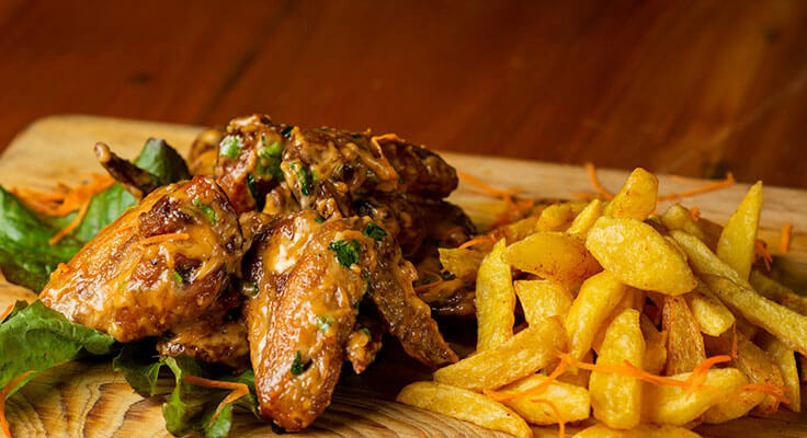 Chicken wings and fries on wooden platter.