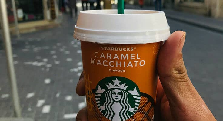 Hand holding Starbucks Caramel Macchiato cup.
