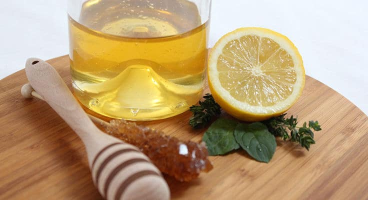 Honey, lemon, and herbs on a wooden surface.