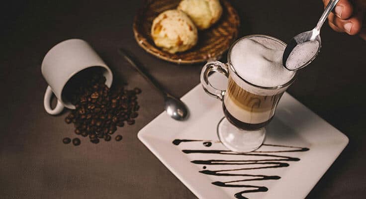Coffee cup, spilled beans, dessert on plate.