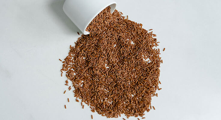 Spilled cup of brown rice on white surface
