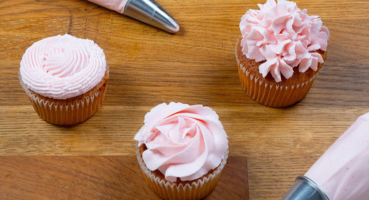Cupcakes with pink frosting on wooden table.