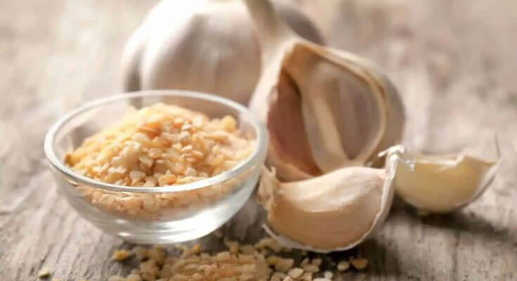 Minced garlic in bowl with garlic cloves.