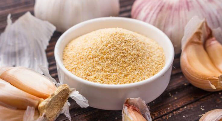 Bowl of garlic powder surrounded by garlic cloves.