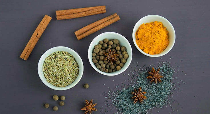 Various spices in bowls with cinnamon sticks.