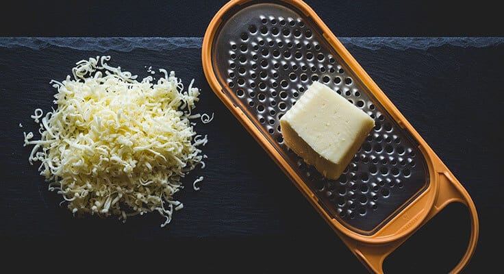 Grated cheese and cheese grater on dark background.