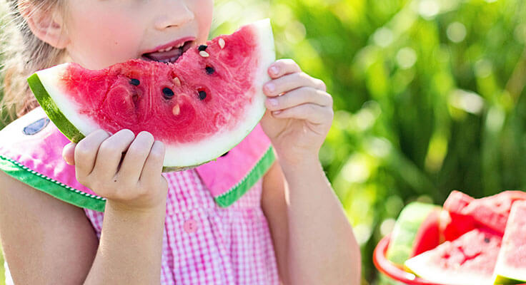 Child eating a slice of watermelon outdoors.