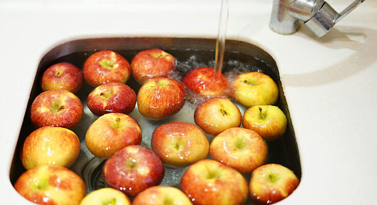 Apples being washed in a kitchen sink.